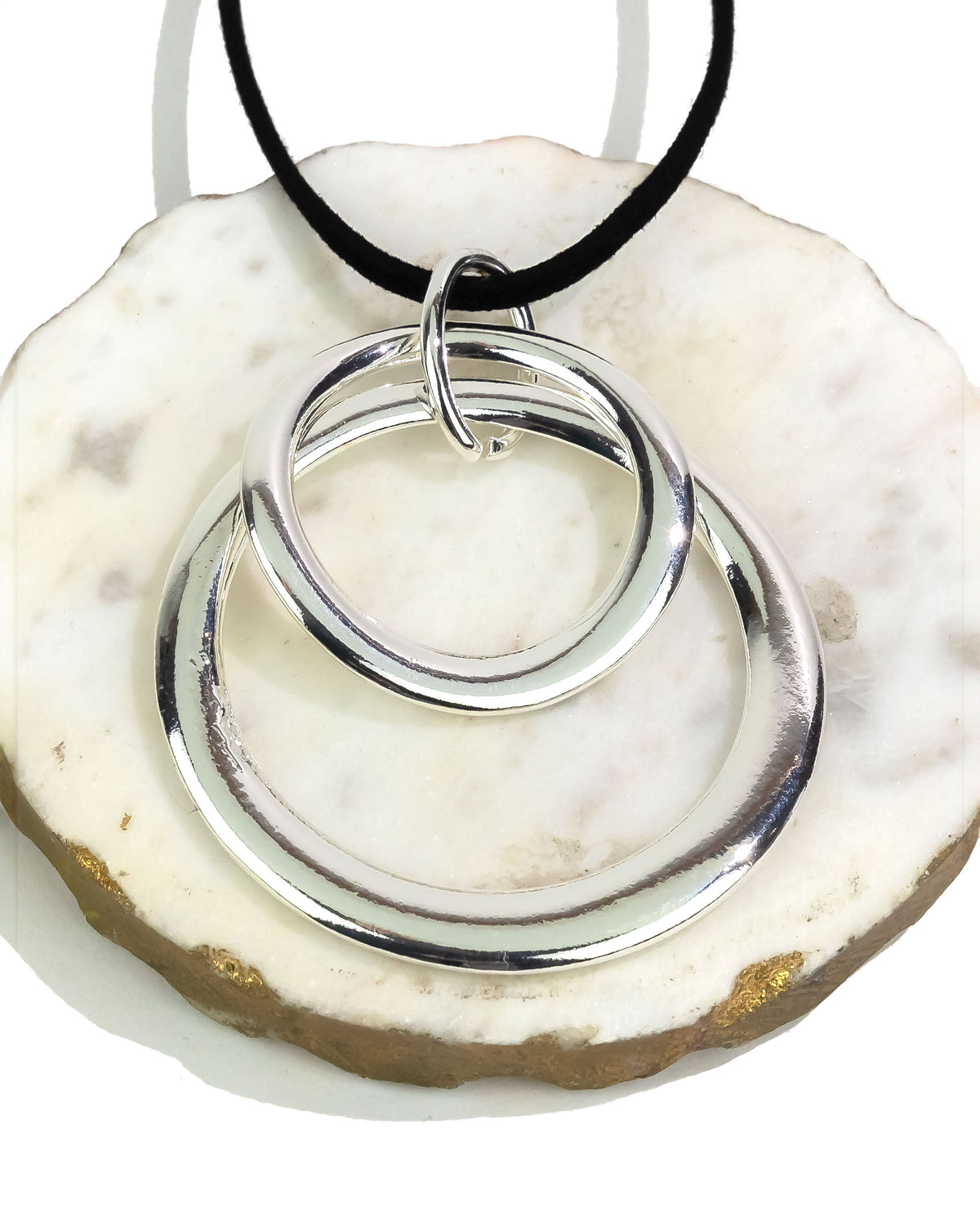 Silver double-circle pendant on a black cord against a white stone background