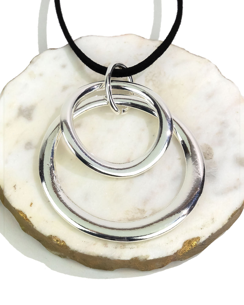 Silver double-circle pendant on a black cord against a white stone background