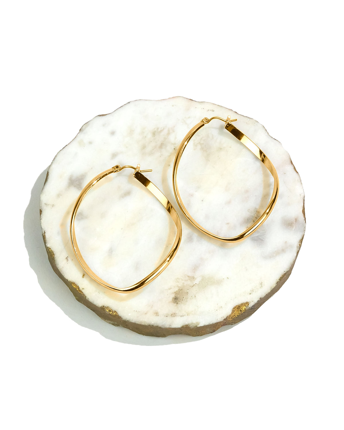 Gold hoop earrings on a white marble surface