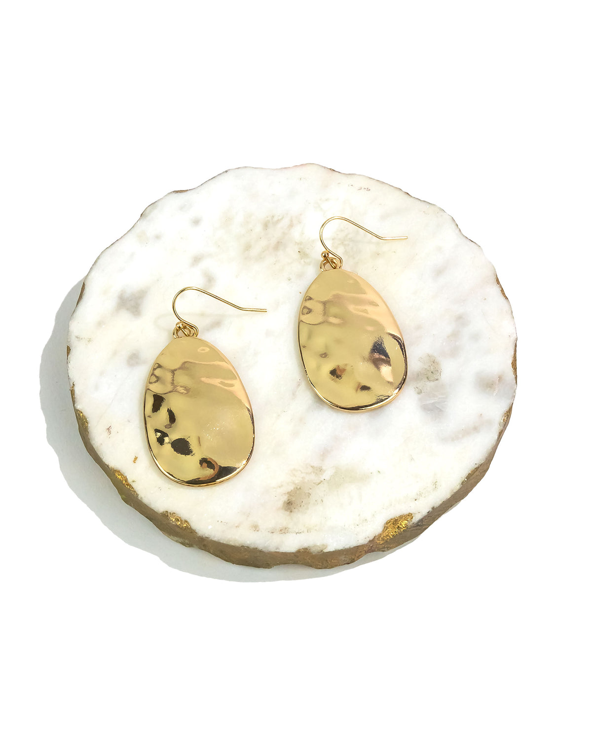 Gold teardrop earrings on a white stone surface