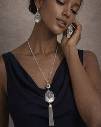 Woman wearing silver jewelry with a necklace and earrings against a neutral background