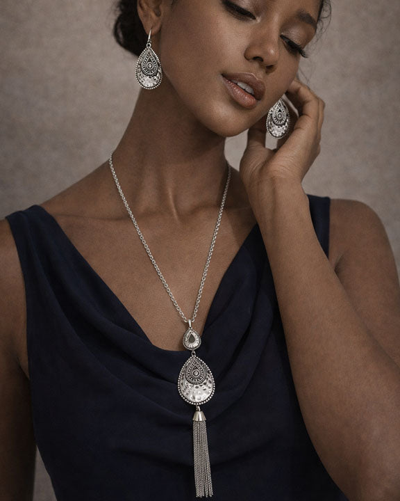 Woman wearing silver jewelry with a necklace and earrings against a neutral background