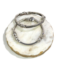 Set of two sectional decorative stretch silver bracelets on a white stone surface