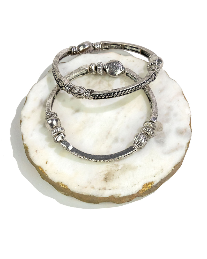 Set of two sectional decorative stretch silver bracelets on a white stone surface