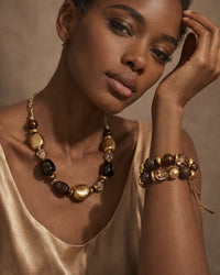 Woman wearing a gold necklace and bracelet against a neutral background